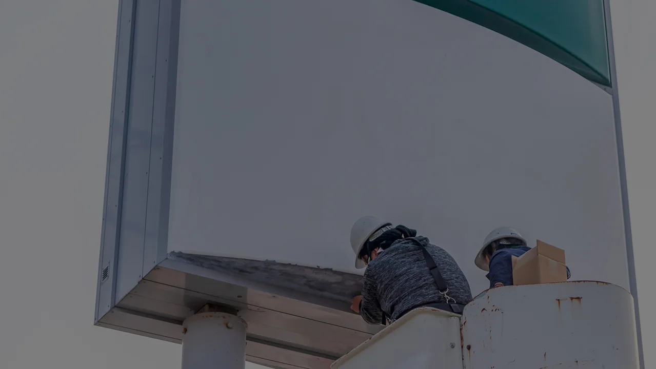 豊富なノウハウを活かし、専門スタッフが高所で看板を丁寧に施工している様子。